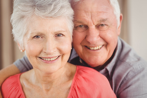 Woman with short hair and coral shirt smiling with husband in blue shirt behind her