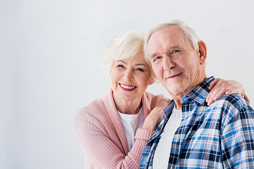 Woman with pink sweater holding the shoulders of a man in blue plaid shirt, both smiling